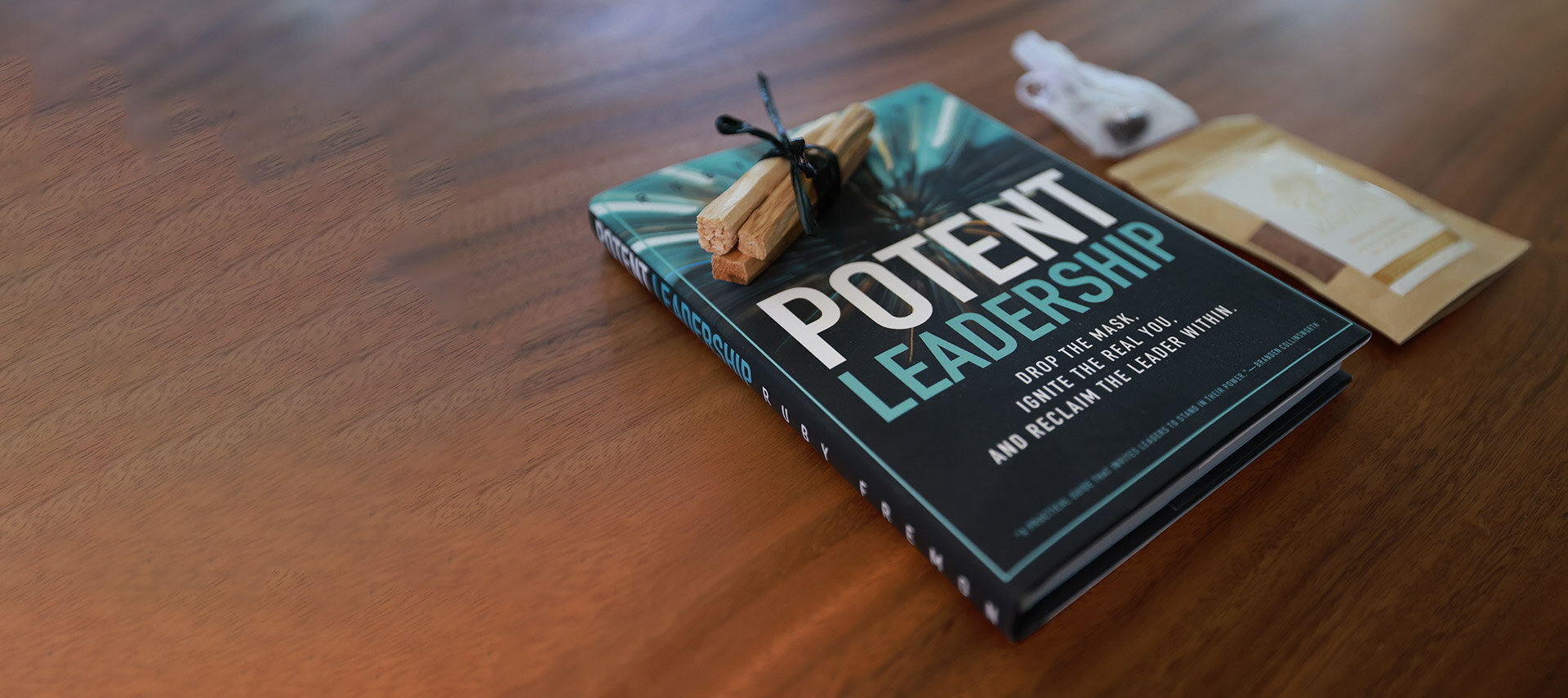 A hardback copy of Potent Leadership lying face up on a walnut table beside a tied bundle of palo santo sticks.