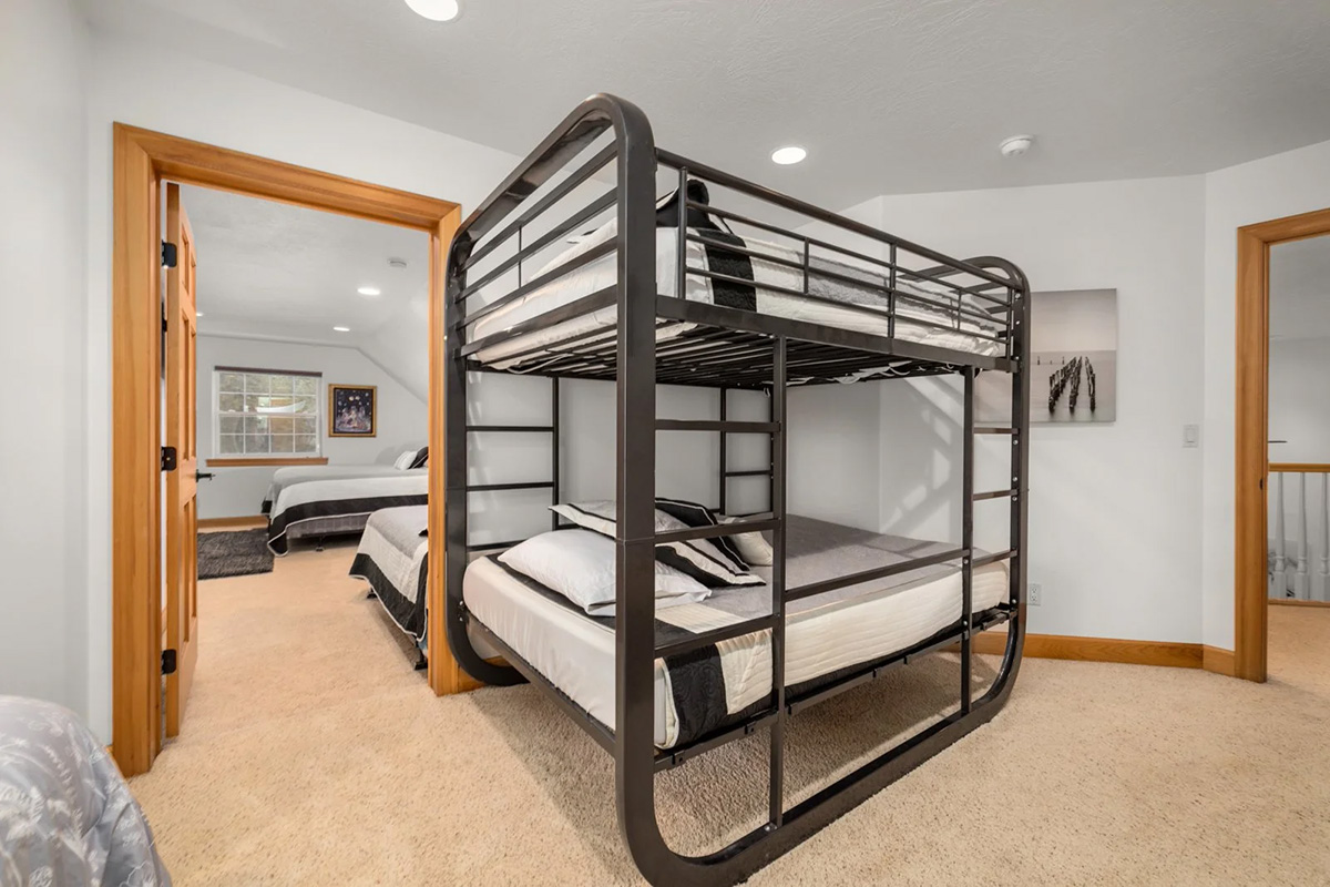 The main lodge&rsquo;s bunk room: a black steel bunk with two full-size berths made up in white, and a further bedroom visible through the open door beside it.
